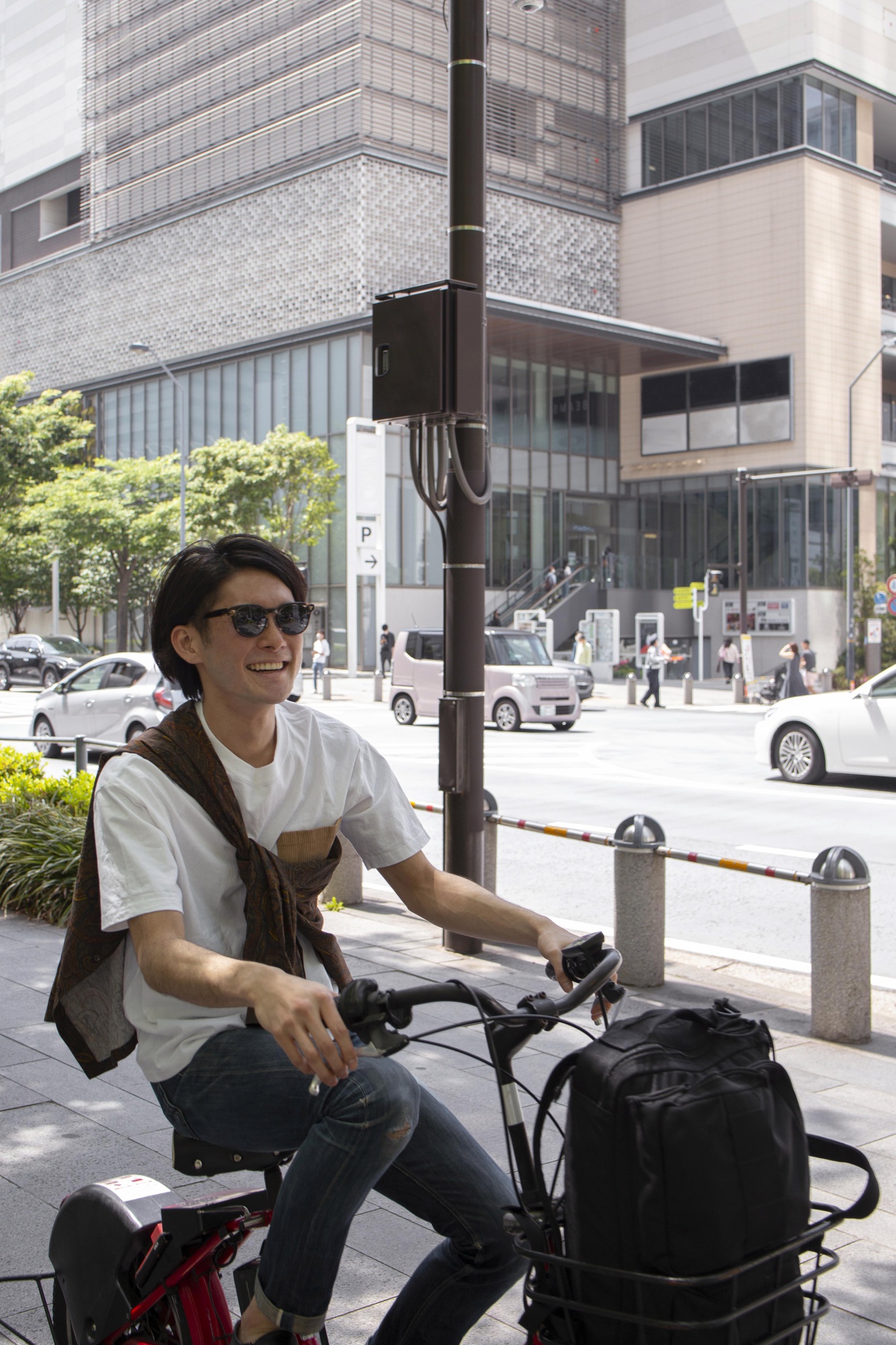サングラスをかけた男性が晴れた街路でオフィスビルの前を自転車で通り過ぎる様子